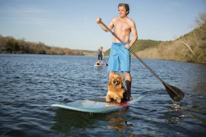 Un hombre parado en un paddleboard con un perro.