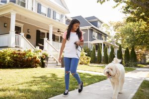 Chica paseando a un perro por una calle suburbana