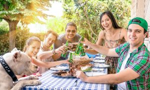 Gruppe glücklicher Freunde, die am Gartengrill essen und anstoßen - Konzept des Glücks mit jungen Menschen zu Hause, die gemeinsam Essen genießen